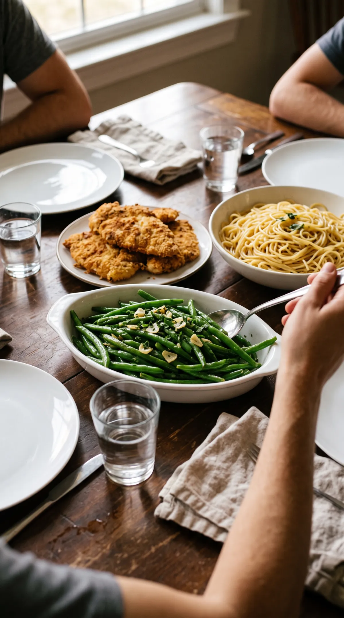Table de dîner avec un plat de haricots verts sautés, du poulet pané, des spaghettis et des verres d'eau